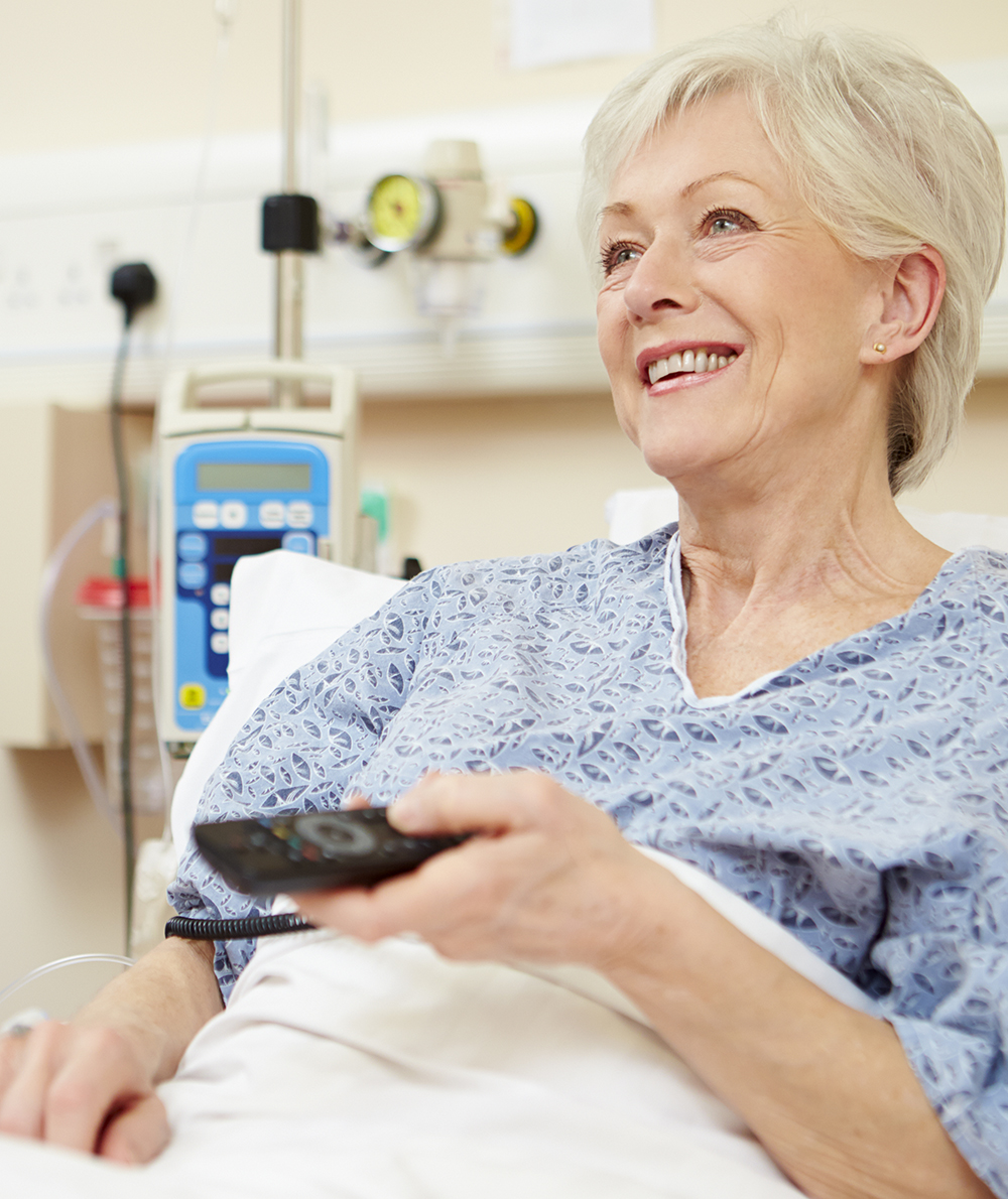 Image of a woman watching TV from her hospital bed.